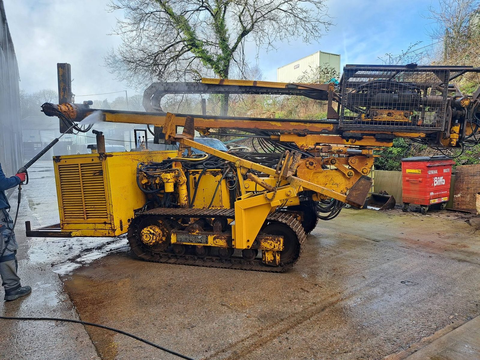 Tracked drilling rig before, with worn yellow paint and rust